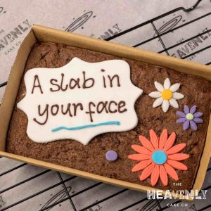 A letterbox brownie decorated with the piped message "a slab in your face" and some colourful flowers